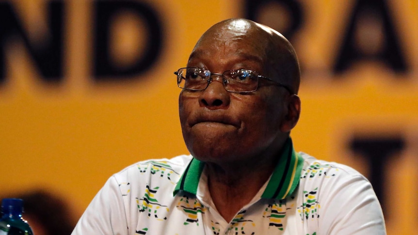 Jacob Zuma sits at a table with a disappointed look on his face.