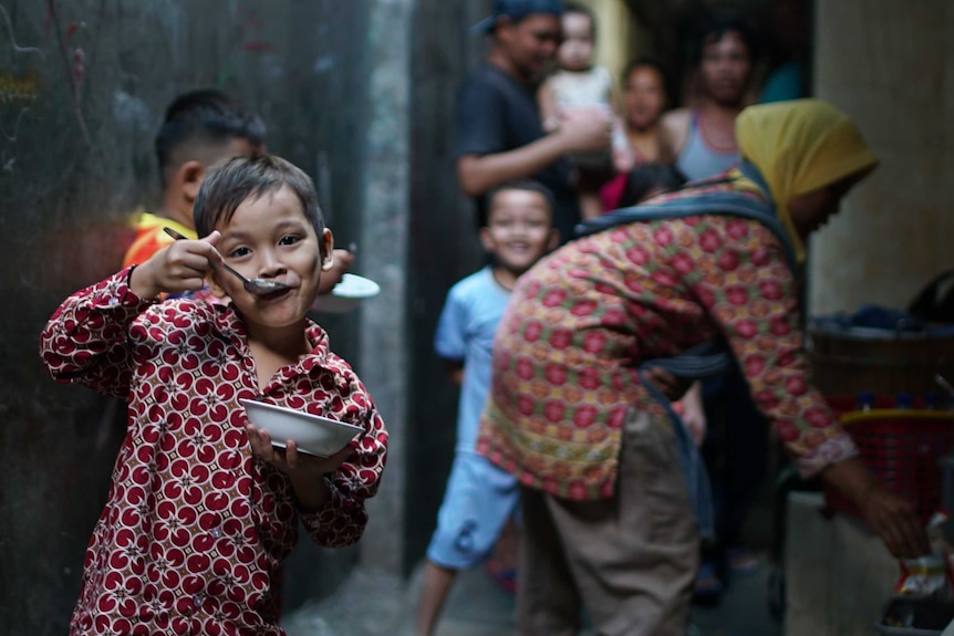 Child eating in the Tambora slum with other children in the background.