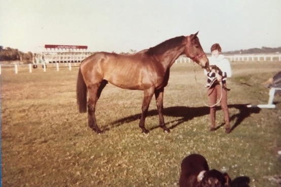 A film photograph of a woman in a white shirt holding the reins of a brown racehorse.