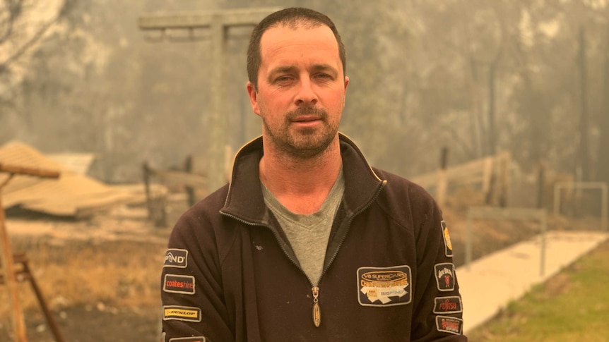 Julian Davies, a man in a black top, looks at the camera through a smoky yellow haze.