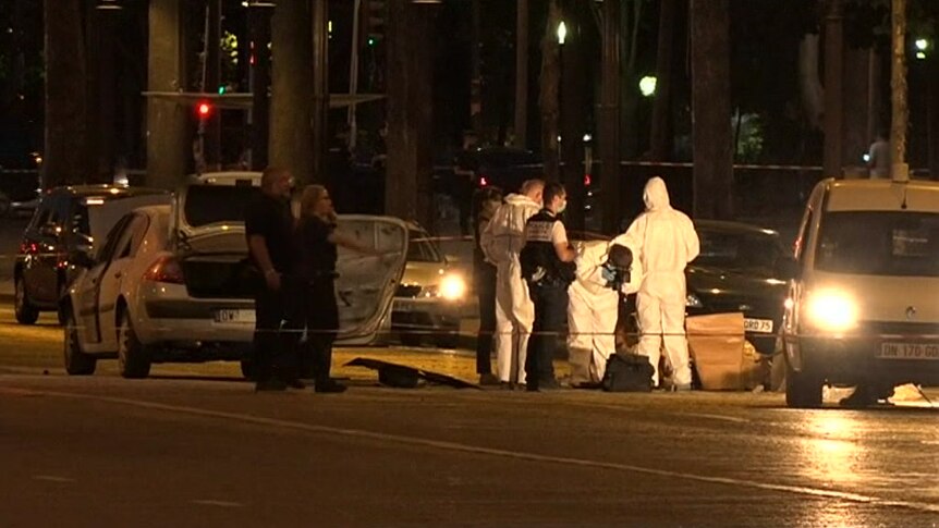 Police officers carry out forensic examination of a car at night.