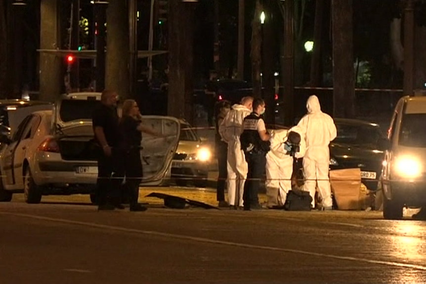 Police officers carry out forensic examination of a car at night.