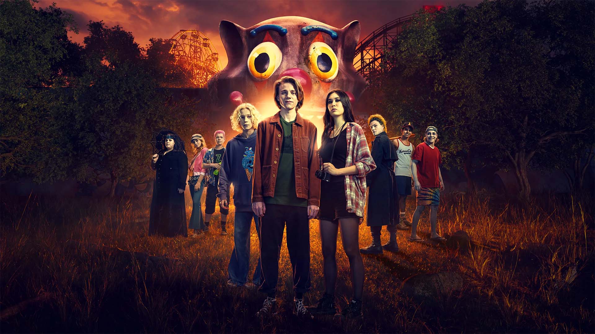 An ensemble of teens in front of a spooky theme park at night