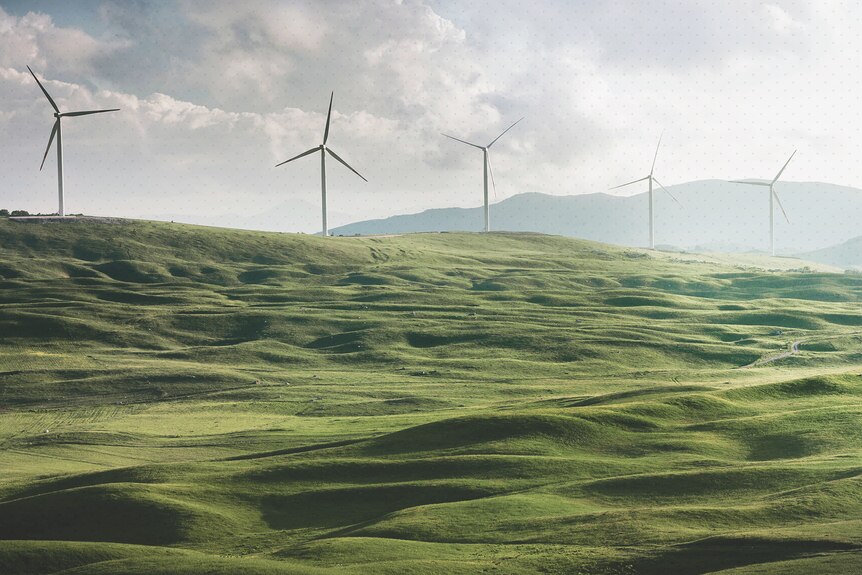 A landscape photo of rolling green hills, atop which stand wind turbines.