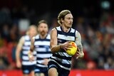 A Geelong defender looks upfield as he holds the ball, ready to deliver a kick.