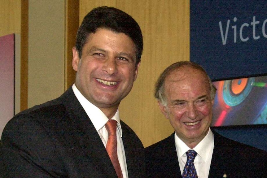 Three men smile and shake hands inside a conference room.