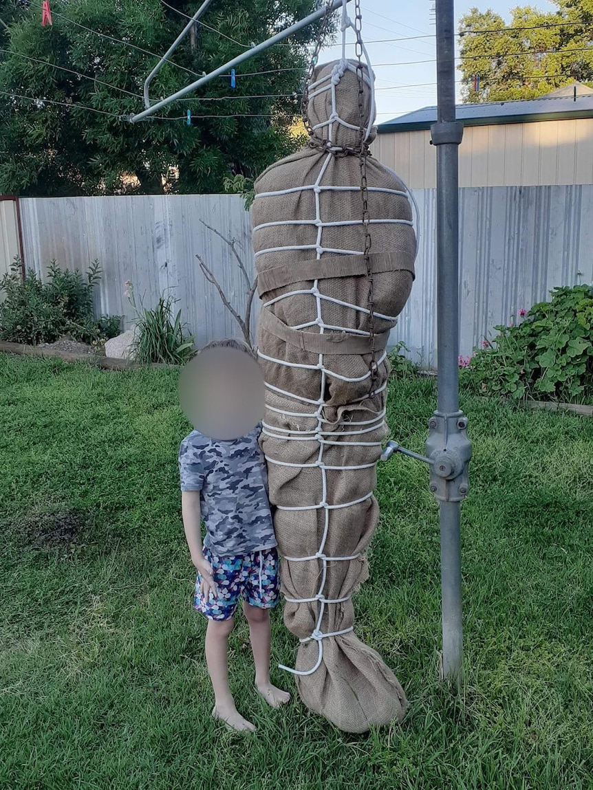 Boy with blurred face standing next to burlap wrapped figure handing clothesline.