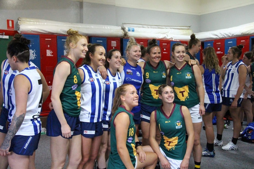 A group of AFLW players smile and pose for a photo in a locker world.