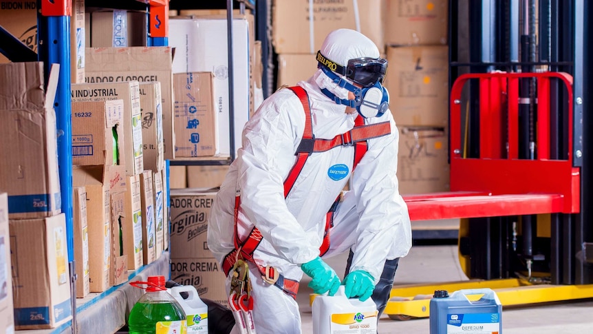 A man wearing protective gear with several bottles of cleaning product.