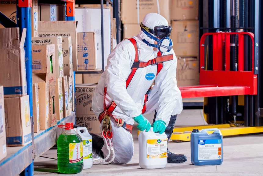 A man wearing protective gear with several bottles of cleaning product.