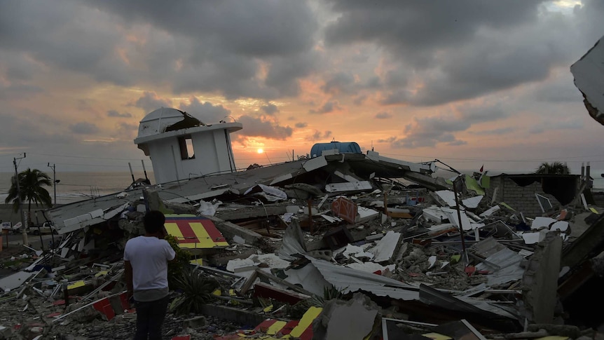 Sun sets as a man stands near rubble in Pedernales