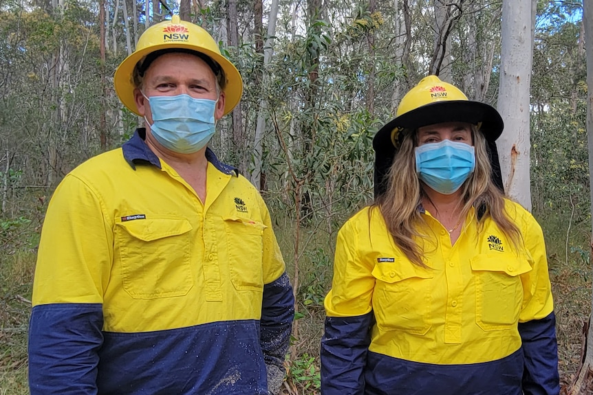A man and a woman in work gear stand in the bush.