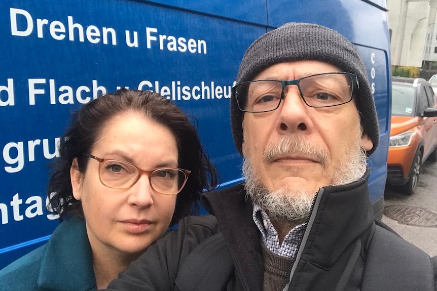 A selfie of a woman and man in beanie in front of blue van