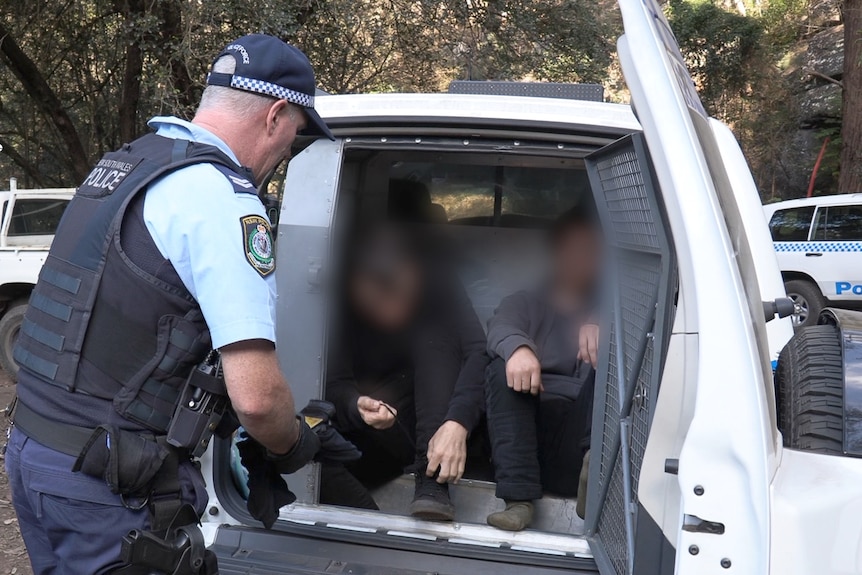 A police officer speaks to two people loaded into the back of a wagon