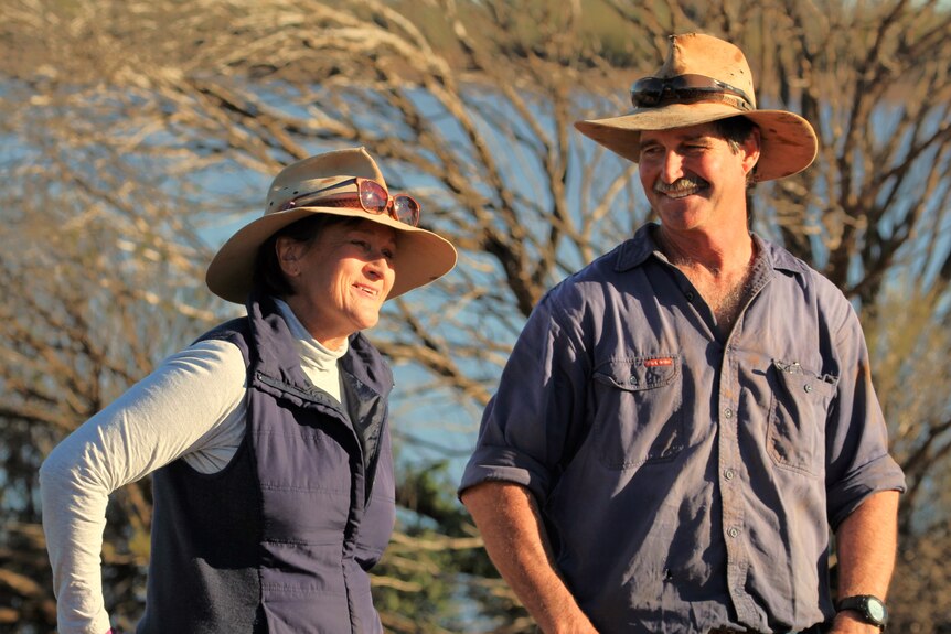 a man and woman in a paddock, the man wears a large hat
