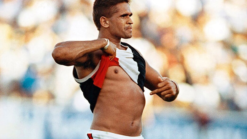 An Indigenous AFL player lifts his shirt and points to the colour of his skin in response to racial vilification by the crowd.