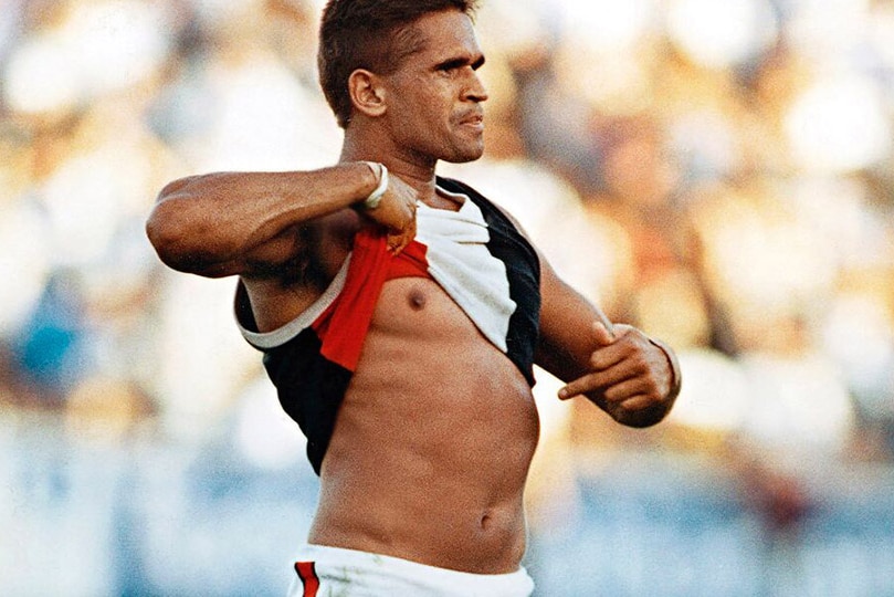 An Indigenous AFL player lifts his shirt and points to the colour of his skin in response to racial vilification by the crowd.