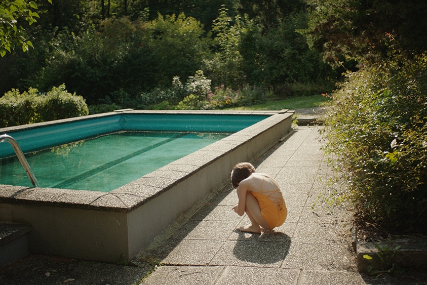 A young AI girl crouched in bathers beside a film in the film The Trouble with Being Born