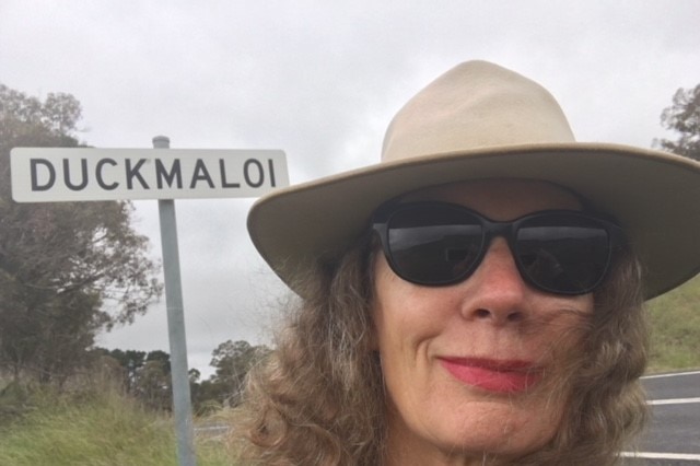 Close up of a woman's face with a sign saying Duckmaloi in the background