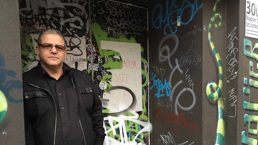 Business owner Sam Conti stands in front of the entrance to his property, which is covered in graffiti tags