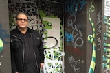 Business owner Sam Conti stands in front of the entrance to his property, which is covered in graffiti tags