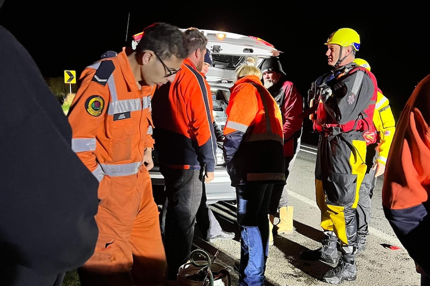 People in emergency services gear stand around truck at nightime.