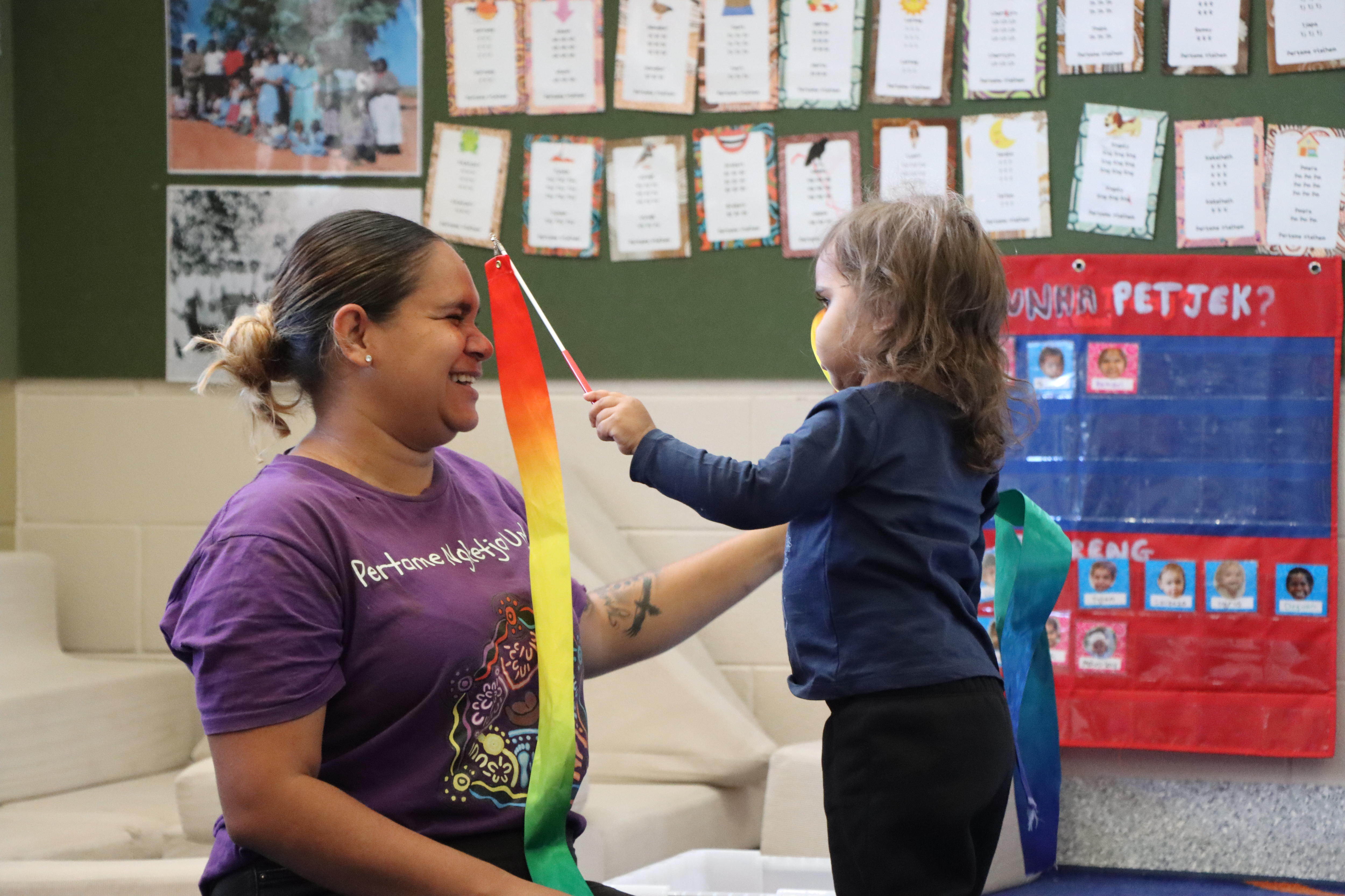 A woman plays with a toddler holding a ribbon.