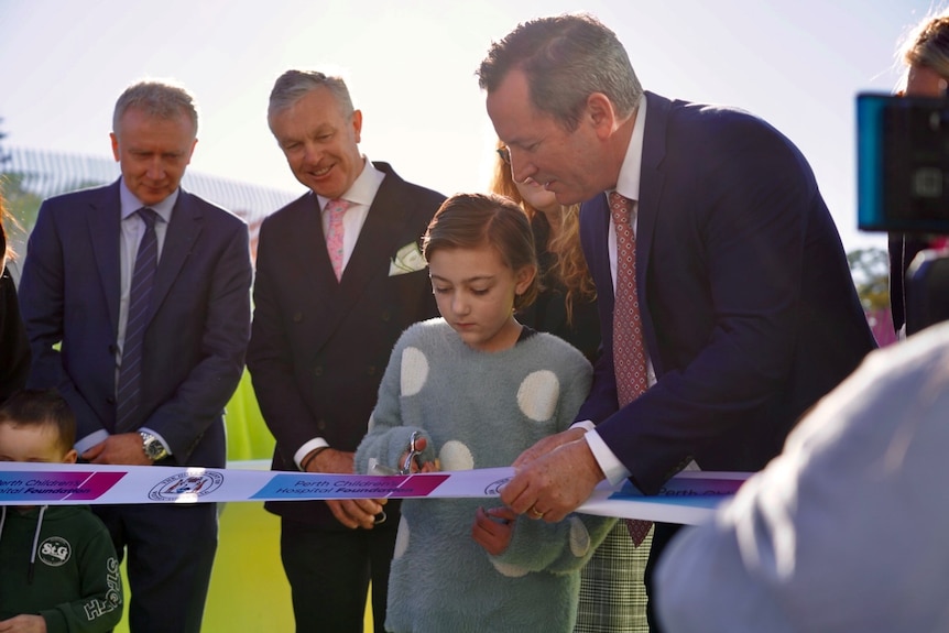 A little girl cuts a ribbon, while three men look on.