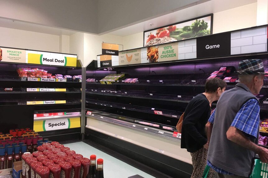 Anonymous elderly man and woman look at empty fresh meat fridges in Woolworths supermarket.