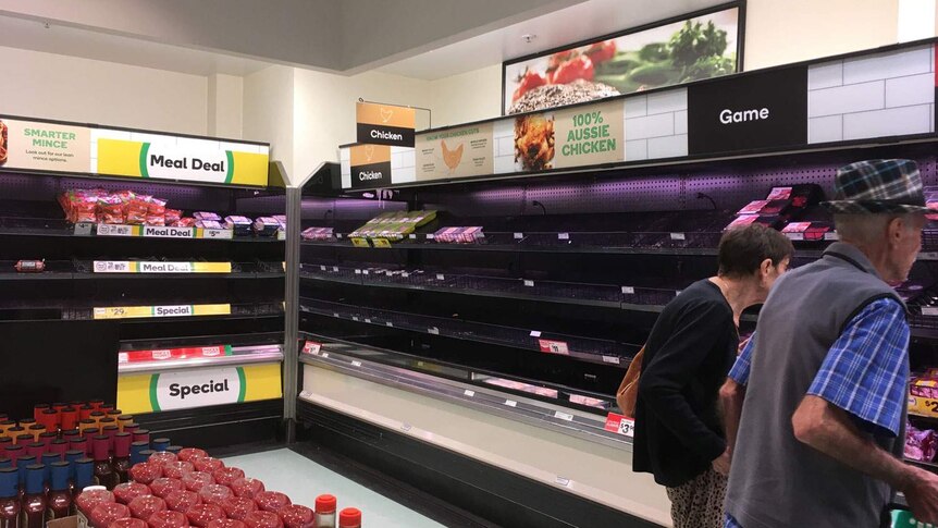 Elderly couple look at empty fresh meat fridges in Woolworths supermarket near Brisbane on March 17, 2020