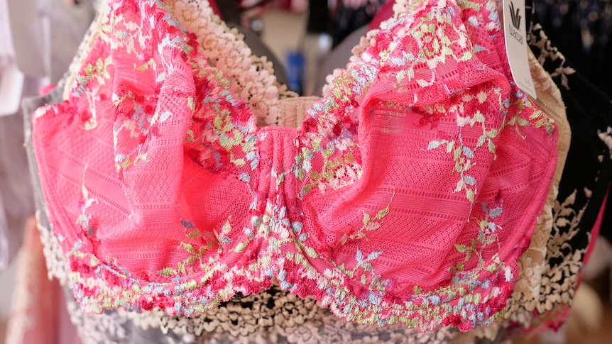 Closeup of a bright pink floral lacey bra hanging on a rack. 