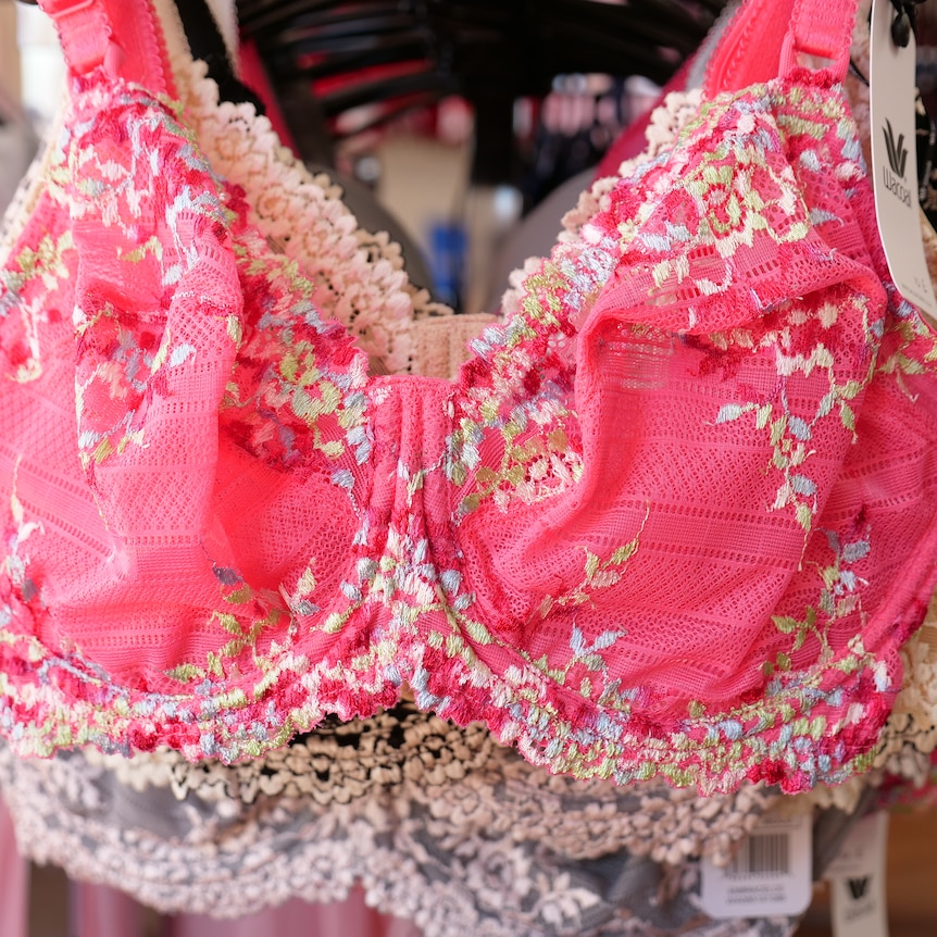Closeup of a bright pink floral lacey bra hanging on a rack. 