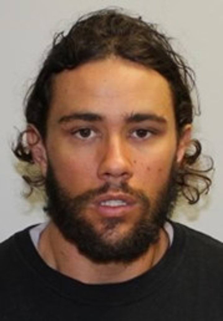 A mug shot of Orpheus Pledger with brown hair tied back and a beard in a black shirt. 