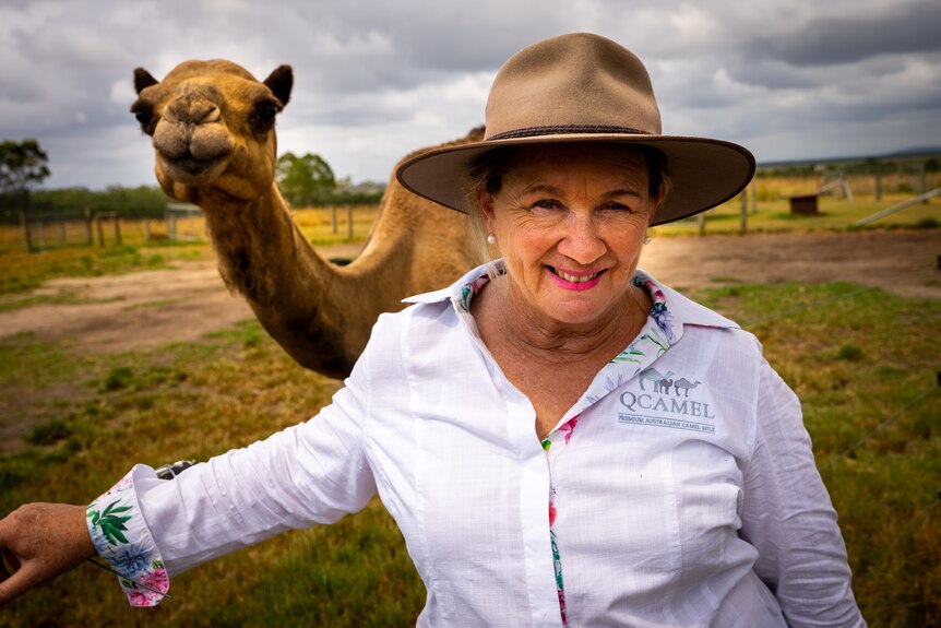 Photo of a woman smiling in front of a camel.