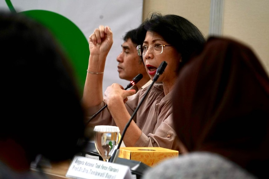 A woman gestures as she speaks into a microphone at a conference