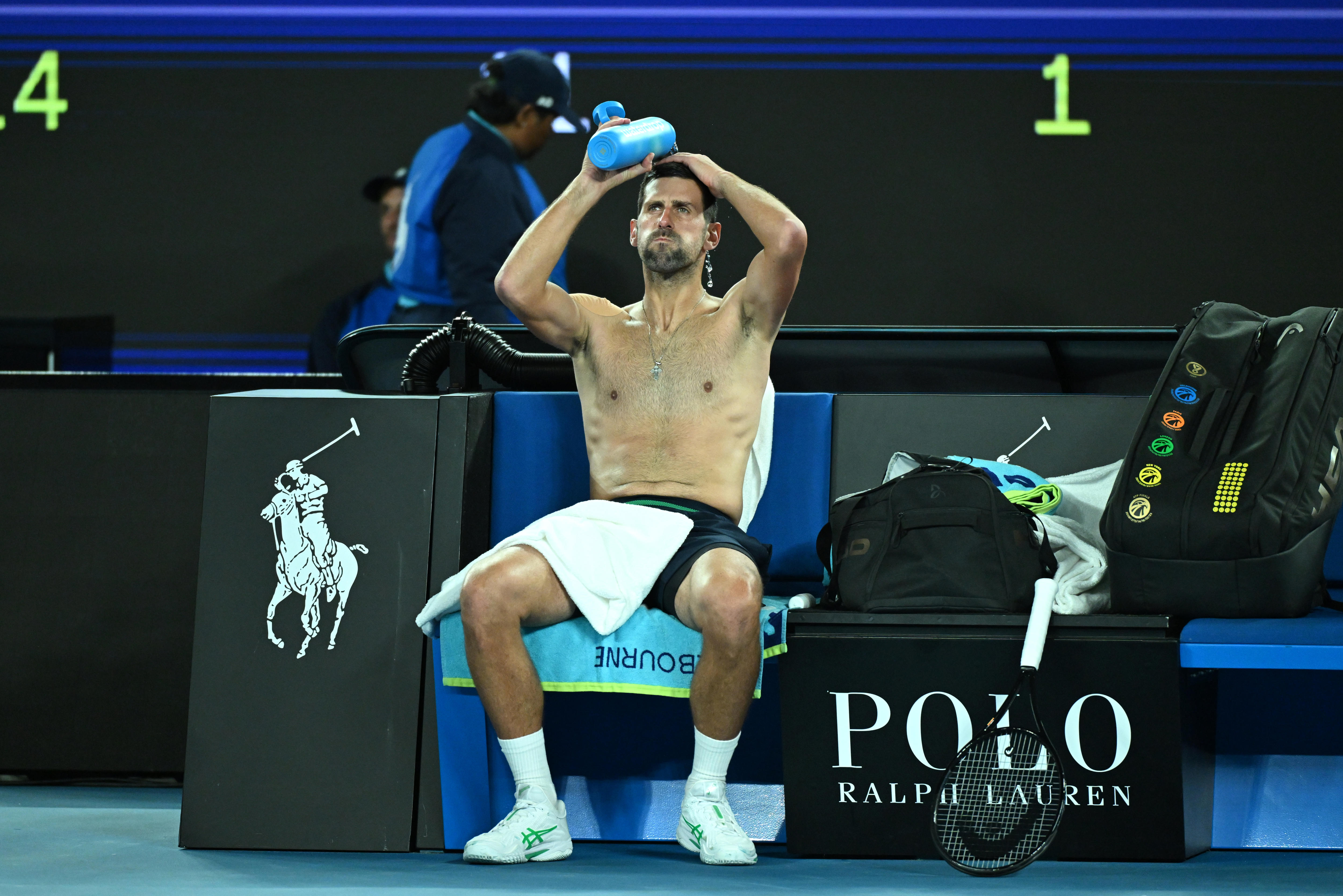 Novak Djokovic se vierte agua de una botella sobre la cabeza mientras está sentado sin camisa en la cancha. 