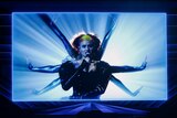 An Australian performer, Montaigne, performs at Eurovision via video, singing while flanked by backing dancers.