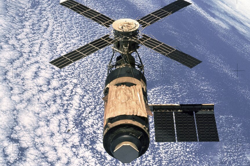 A satellite orbiting the earth with five outstretched solar panel wings.