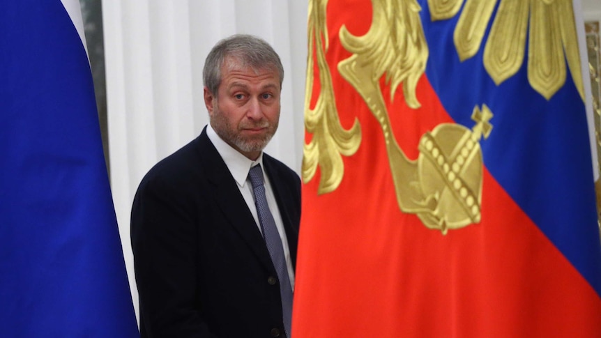 Russian billionaire and businessman Roman Abramovich stands near a Russian flag.