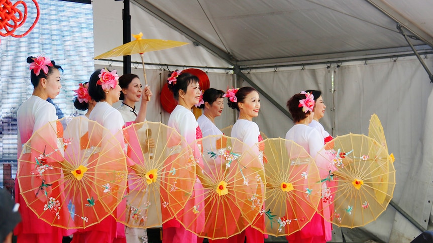 Women with parasols dance on a stage.