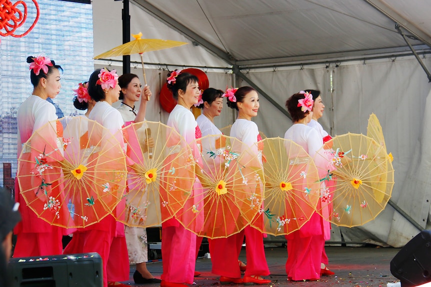 Women with parasols dance on a stage.