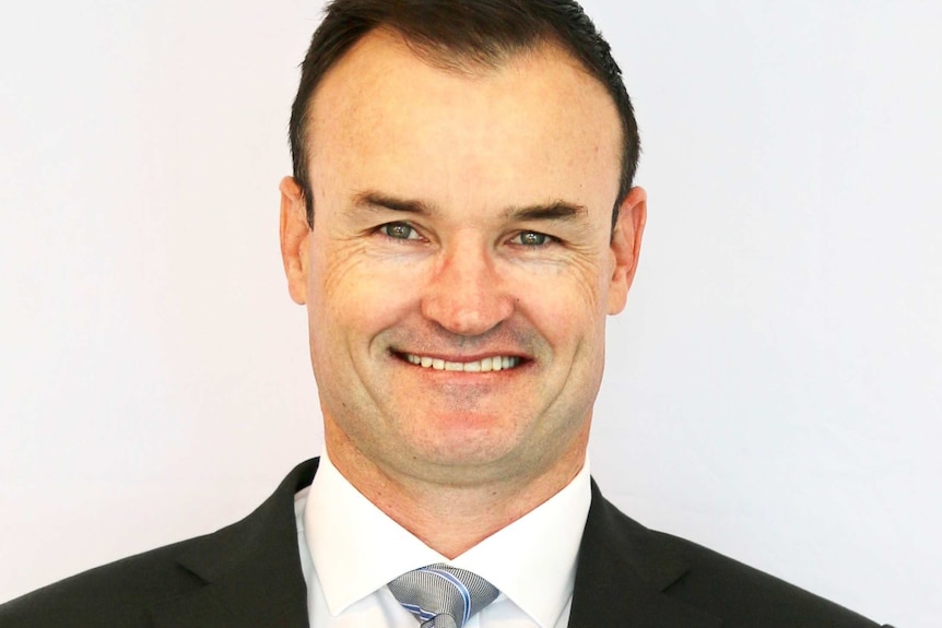 A head and shoulders shot of a middle aged man with short hair smiling for a photo.