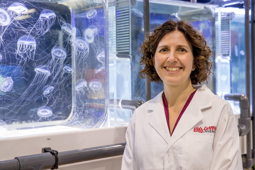 Une femme en blouse de laboratoire se tient devant un aquarium rempli de méduses