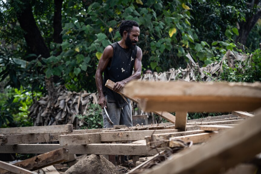 A man pulls his home apart with a pile of wood in the foreground