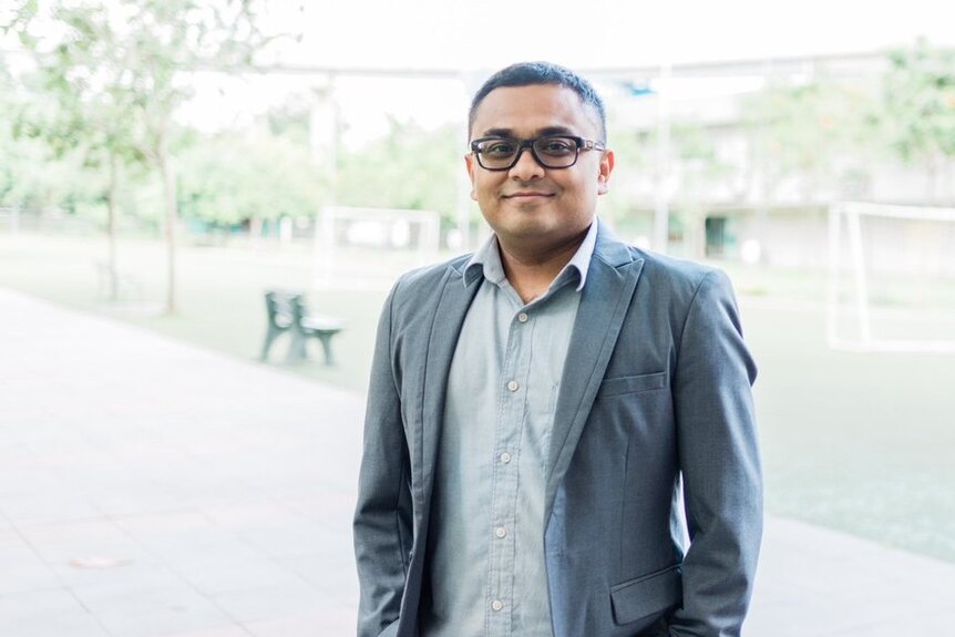 A man wears a suit and glasses while posing for a portrait