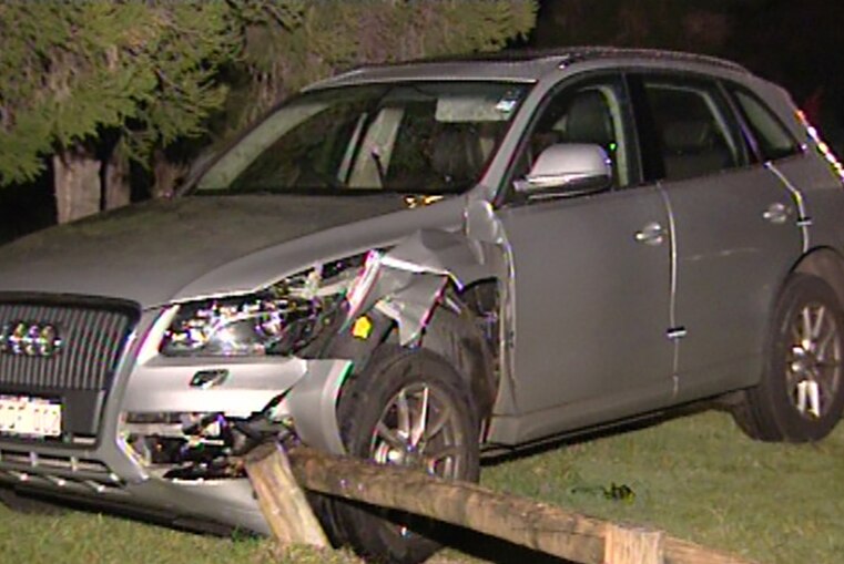 A damaged silver car runs into a low fence.