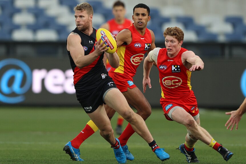 An Essendon forward wheels with the ball in his hands, as a Gold Coast midfielder tries to go after him.