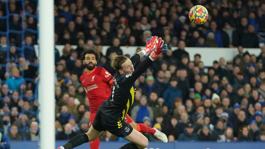 A Liverpool striker looks up as his shot curls past the despairing dive of the Everton goalkeeper into the net.