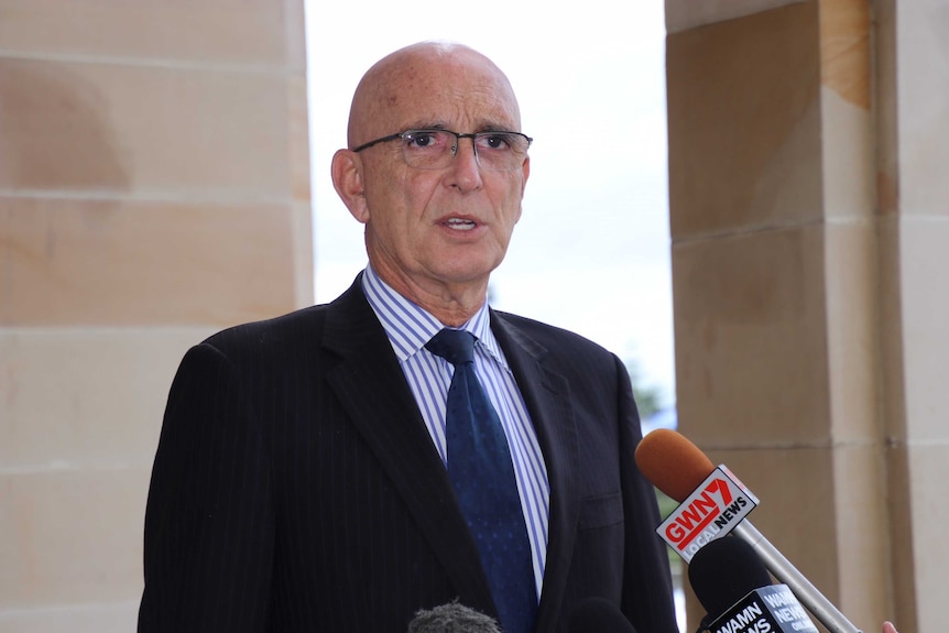 A man in glasses and a suit speaks outside Parliament.