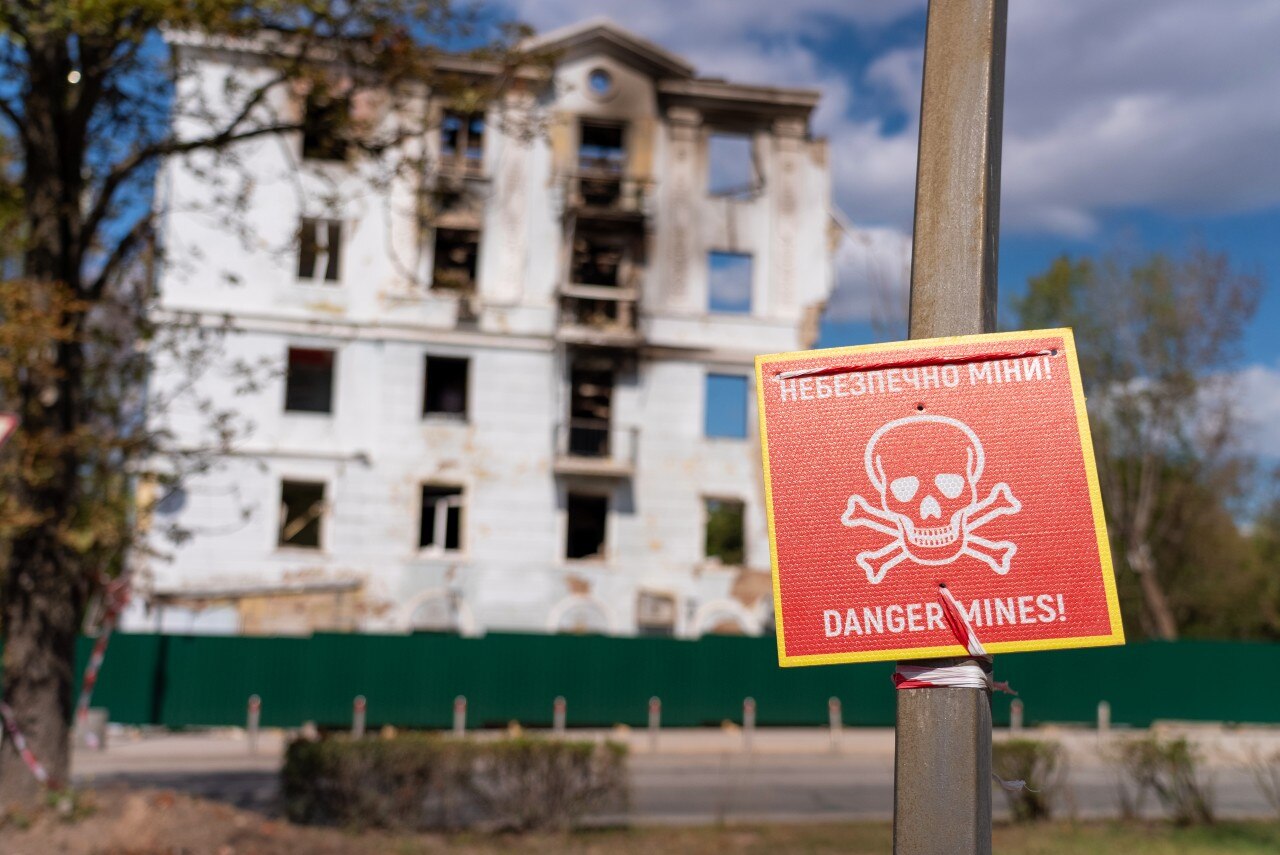 A sign saying 'danger mines' is visible in front of several damaged buildings.